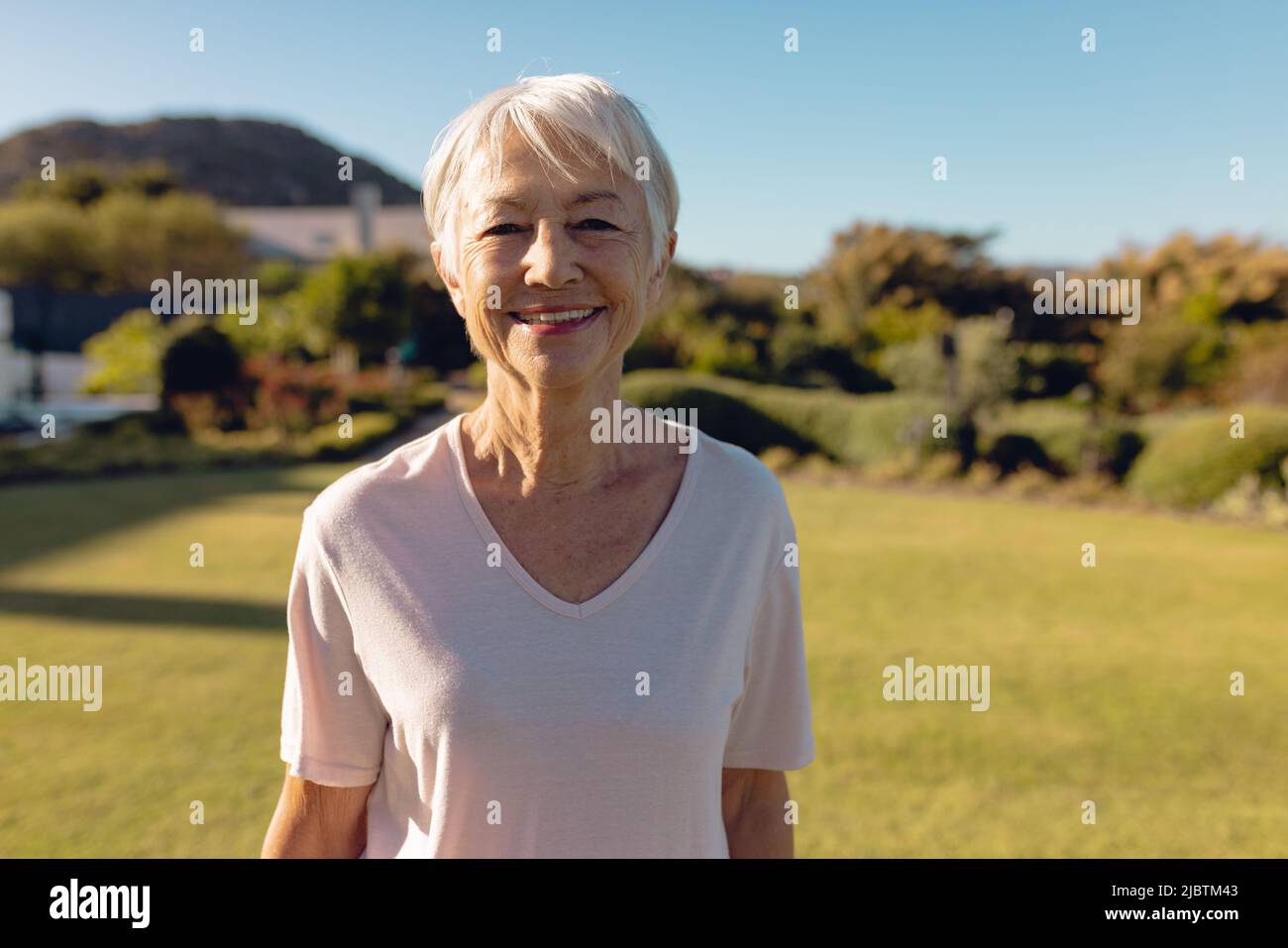 Ritratto di donna anziana asiatica con capelli corti in piedi su terra erbosa contro cielo chiaro in cortile Foto Stock