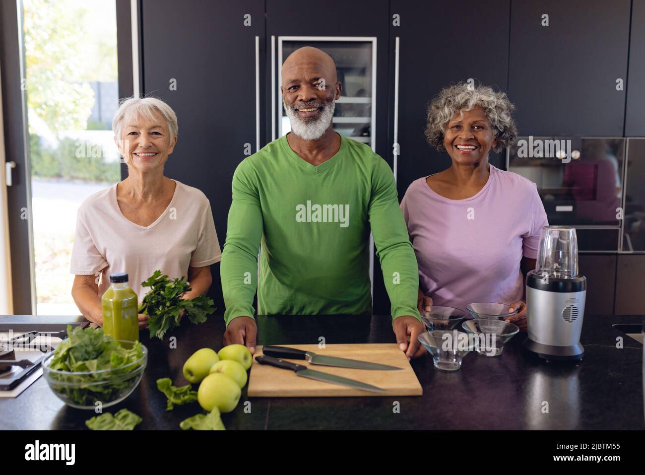 Ritratto di sorridenti amici senior multirazziale facendo frullato di mela e foglia vegetale in cucina Foto Stock