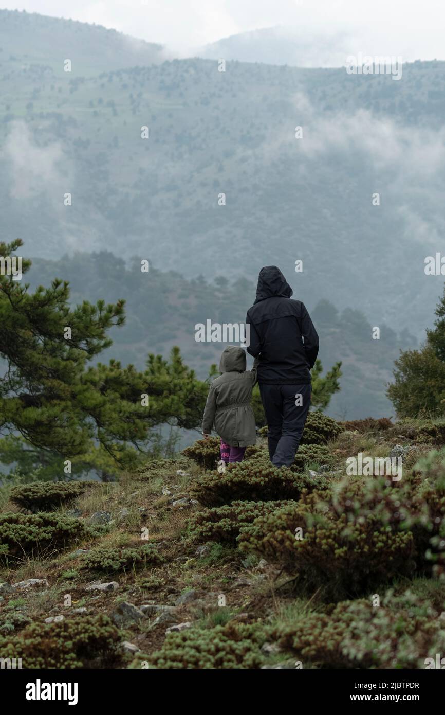 Fuoco selettivo di madre e figlia in piedi sul fianco della montagna in tempo nebbia mentre si guarda il paesaggio. Foto Stock