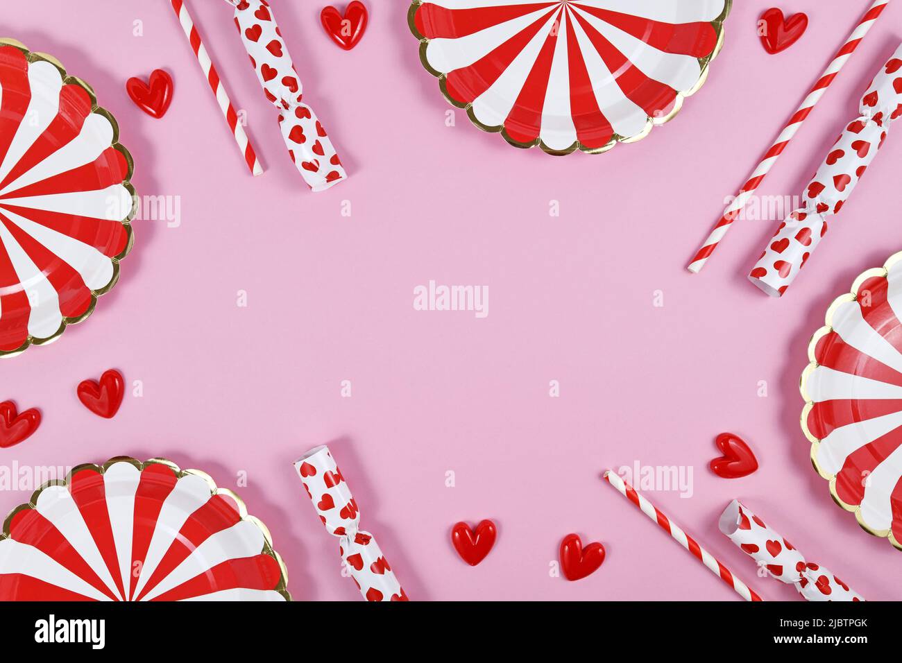 Bordo della festa con piatti di carta rossa, ornamenti di cuore, caramelle e cannucce da bere su sfondo rosa con spazio copia Foto Stock
