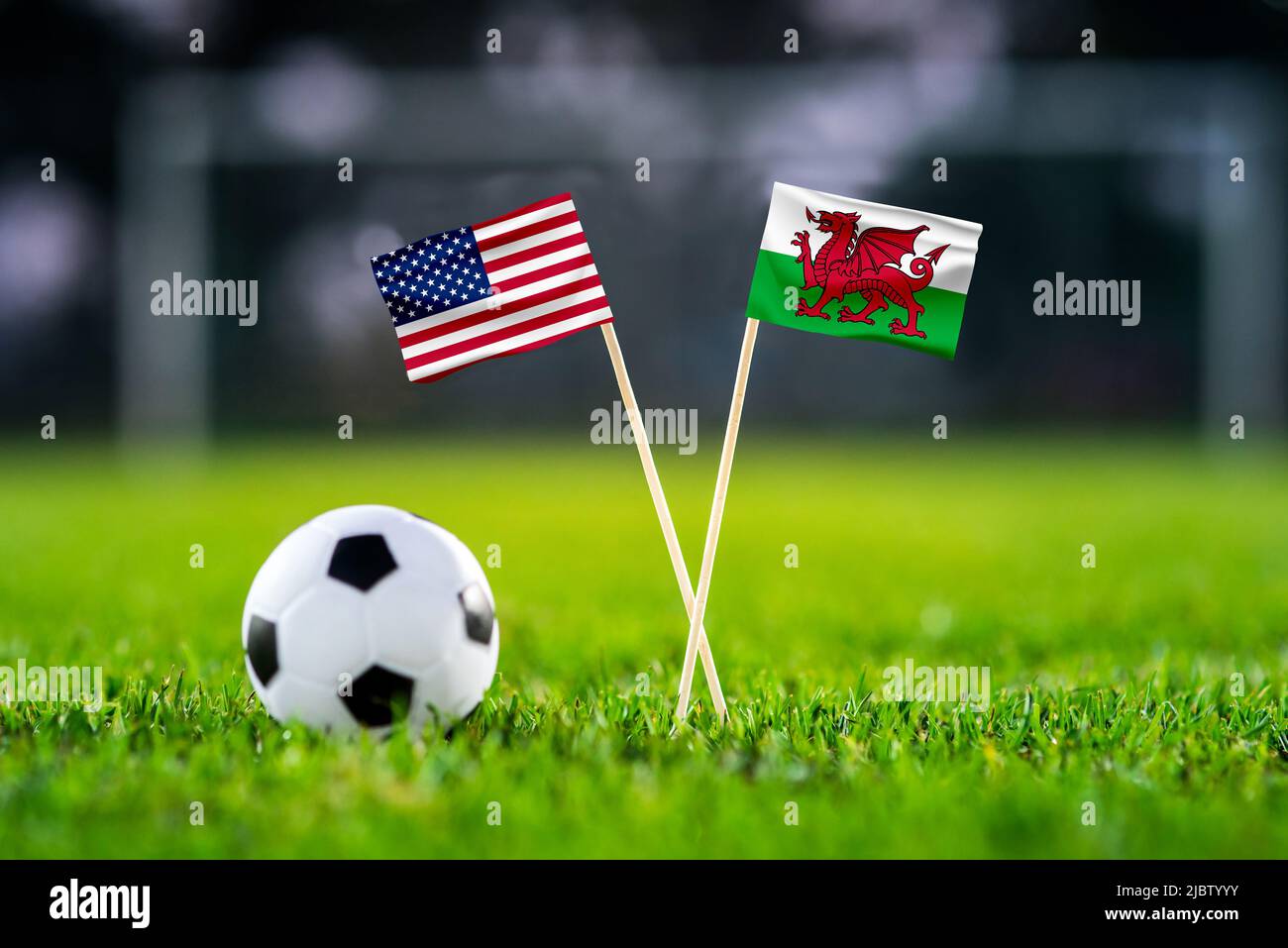 USA vs Galles, Ahmad Bin Ali, carta da parati partita di calcio, bandiere nazionali fatte a mano e palla di calcio su erba verde. Stadio di calcio in background. Nero Foto Stock