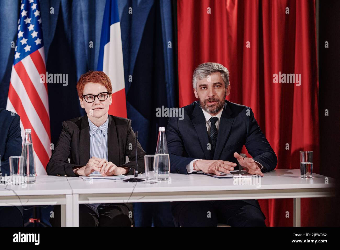 Uomo maturo con capelli grigi che dà il suo rapporto alla conferenza mentre si siede al tavolo con il suo collega Foto Stock