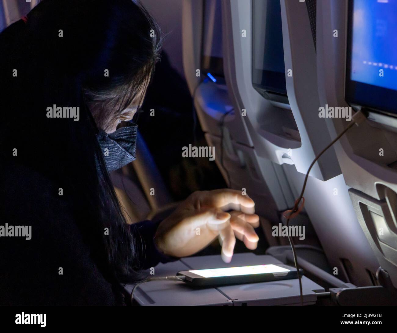 Il passeggero con smartphone in volo notturno è illuminato dalla luce dei display Foto Stock