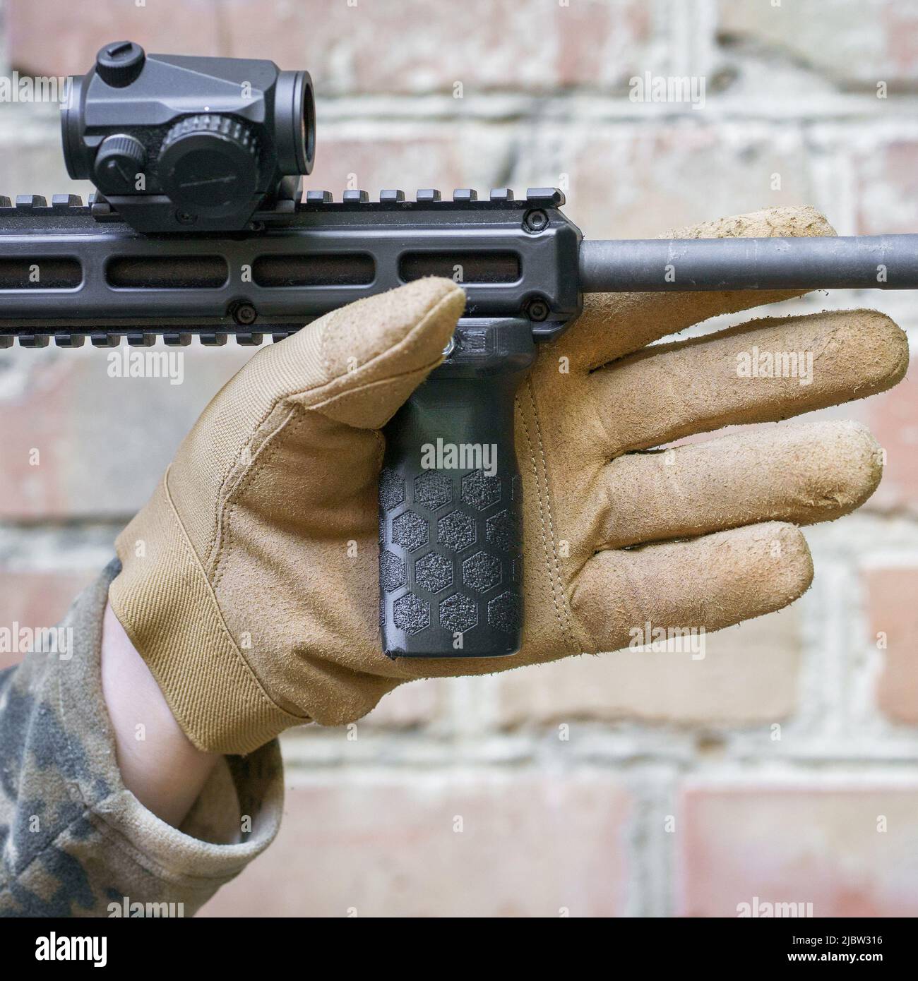 la mano dell'uomo in guanto tattico tiene l'impugnatura anteriore per una pistola del colpo. Pistola im man mano pronta per l'uso. Sparatutto uomo pronto a colpire il bersaglio tenendo una mano impugnatura. Foto Stock