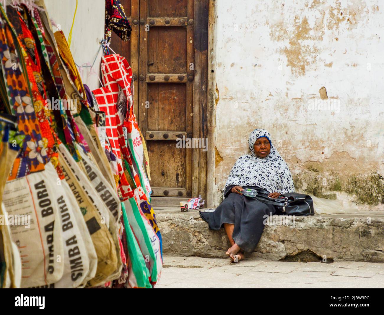 Città di pietra, Zanzibar, Tanzania - Gennaio 2021: Anziana donna africana pensiva seduta tra le mura di pietra della città africana Foto Stock