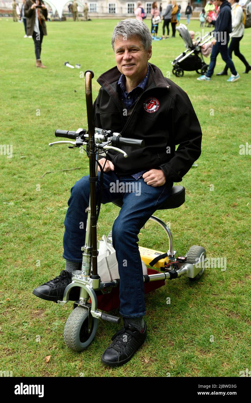 Uomo seduto e che utilizza uno scooter pieghevole (14,8kg, 33 libbre) per la mobilità (Travel Scoot) molto leggero Foto Stock