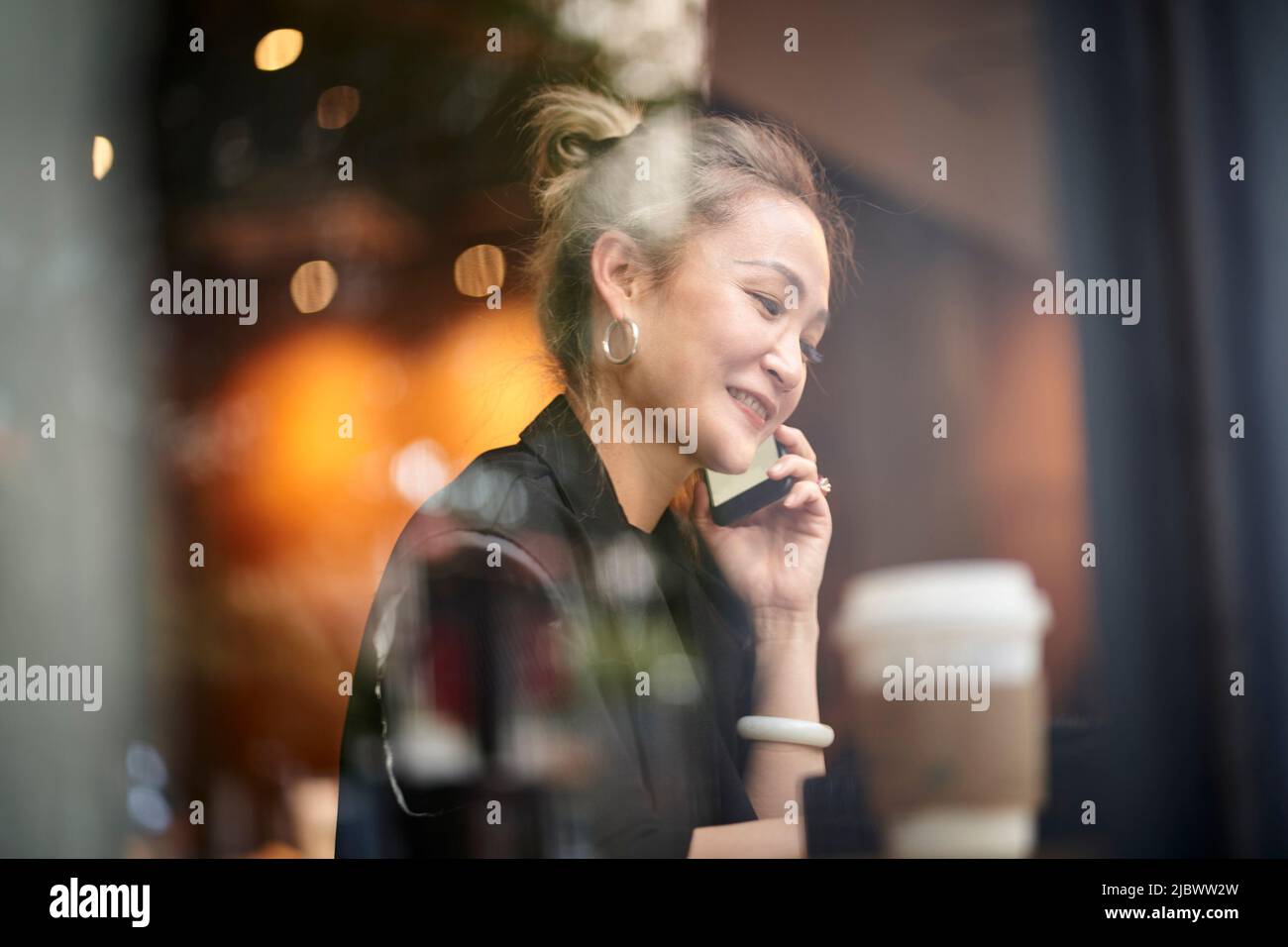 donna asiatica che parla chattando conversando usando il cellulare in caffetteria Foto Stock
