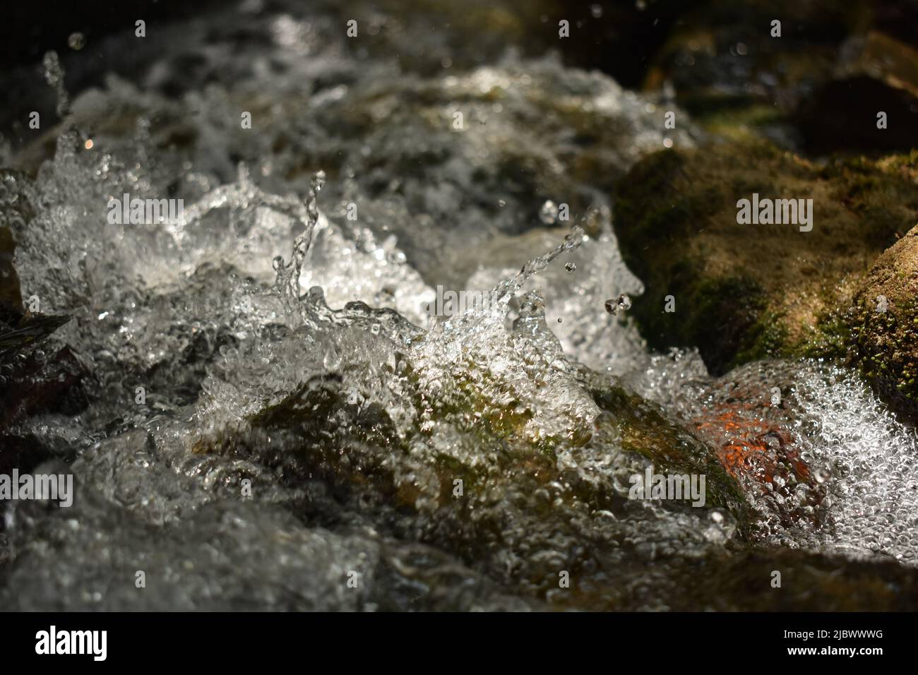 Immagine del flusso d'acqua limpido e delle gocce che spruzzano sulle rocce. Foto Stock