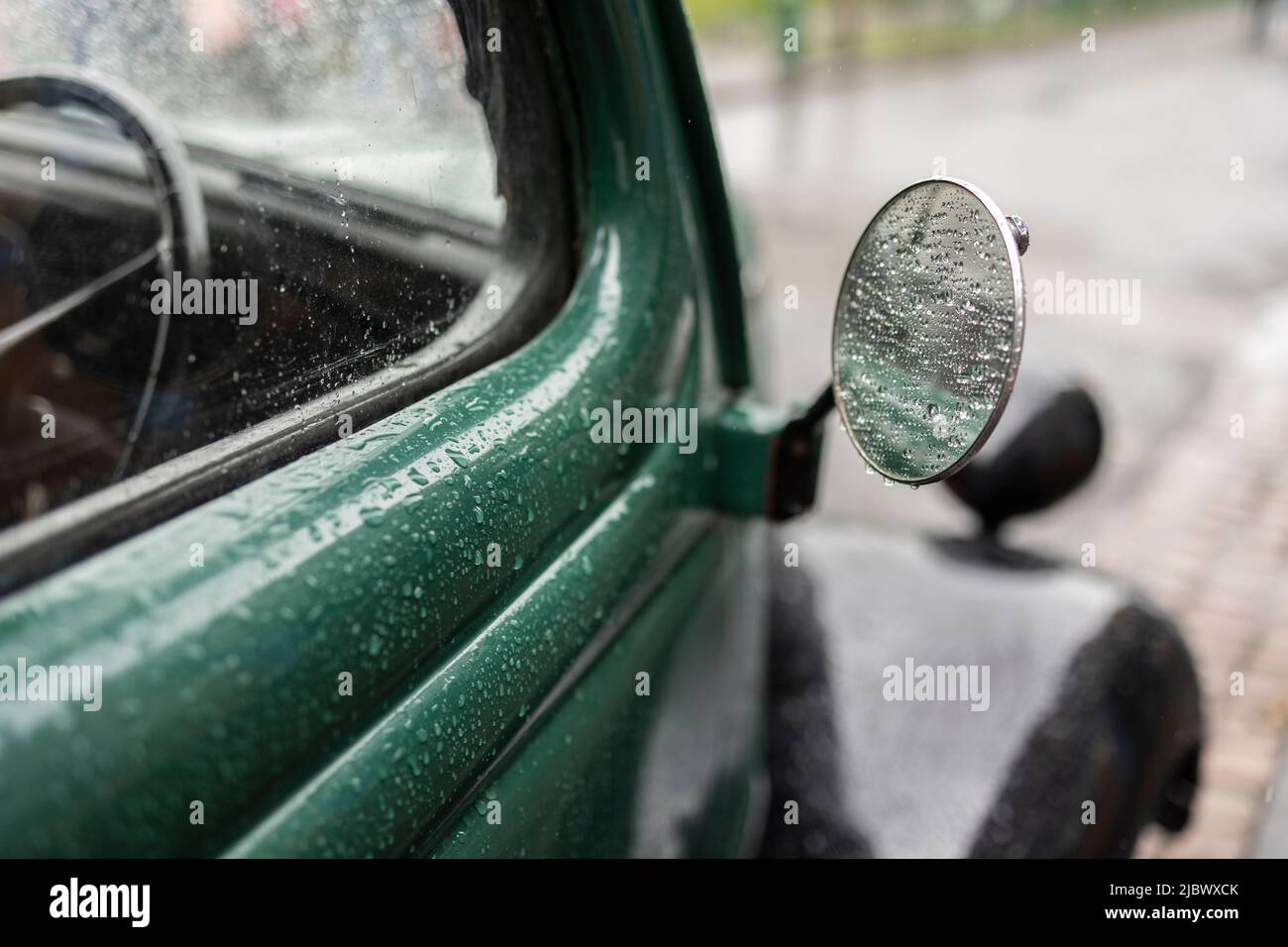 primo piano dello specchio e della porta dell'auto d'epoca verde ricoperta da gocce di pioggia Foto Stock