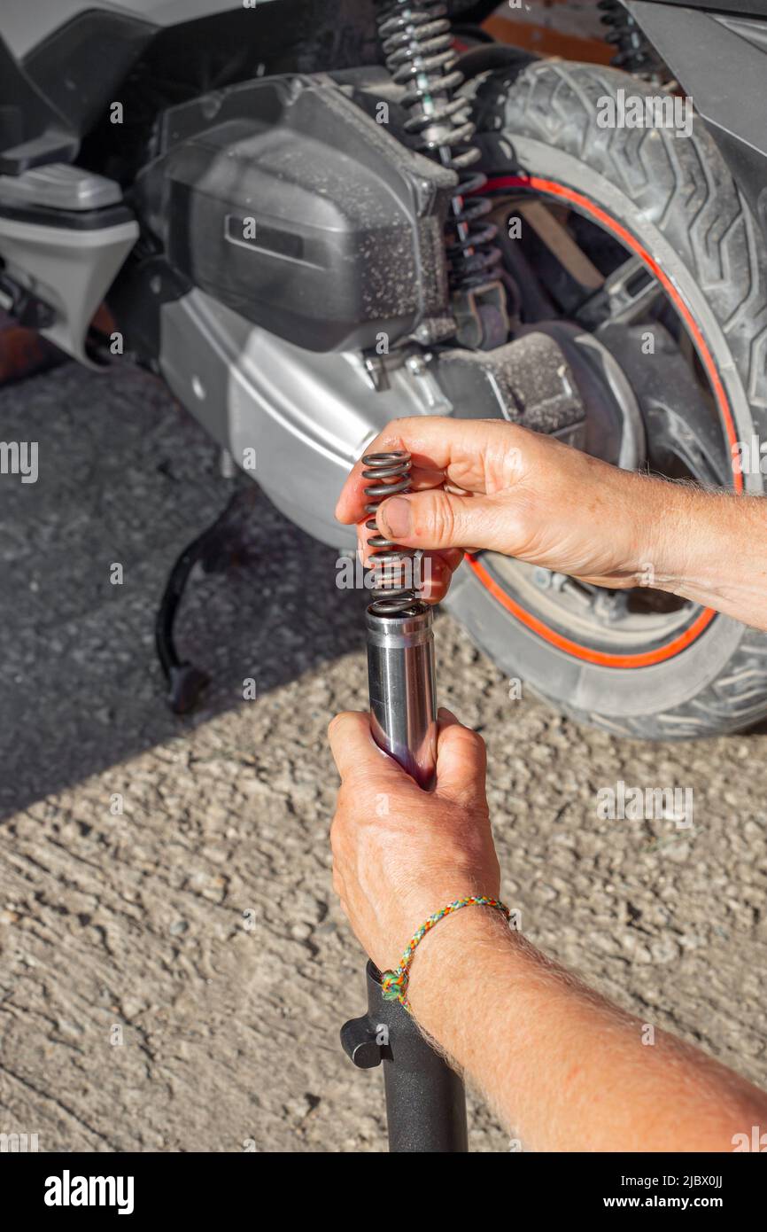 Un meccanico inserisce una molla di smorzamento in metallo nell'ammortizzatore della forcella anteriore di una motocicletta. Manutenzione e riparazione di motocicli. Foto Stock