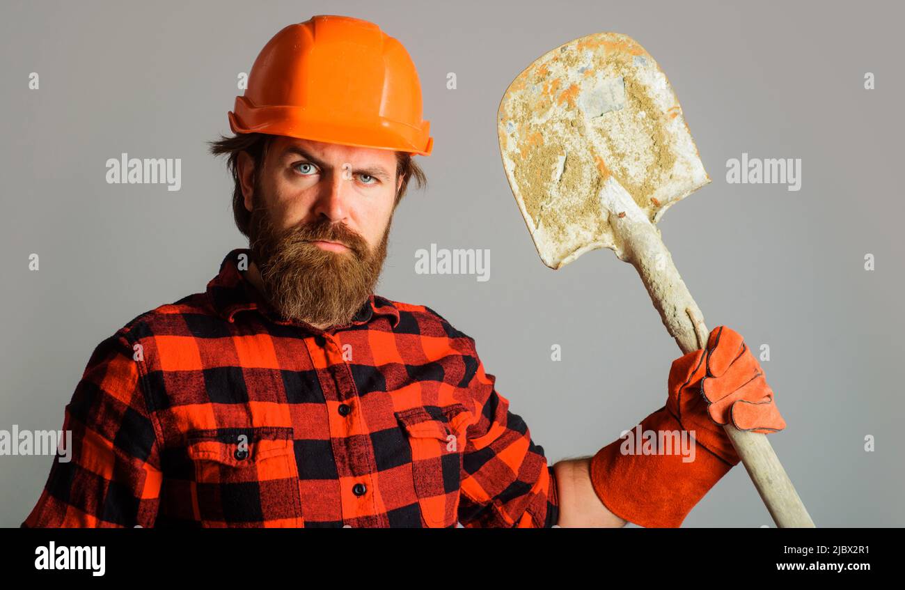 Costruttore serio in elmetto con pala. Uomo da lavoro con batella in guanti da lavoro e casco con lancette. Foto Stock