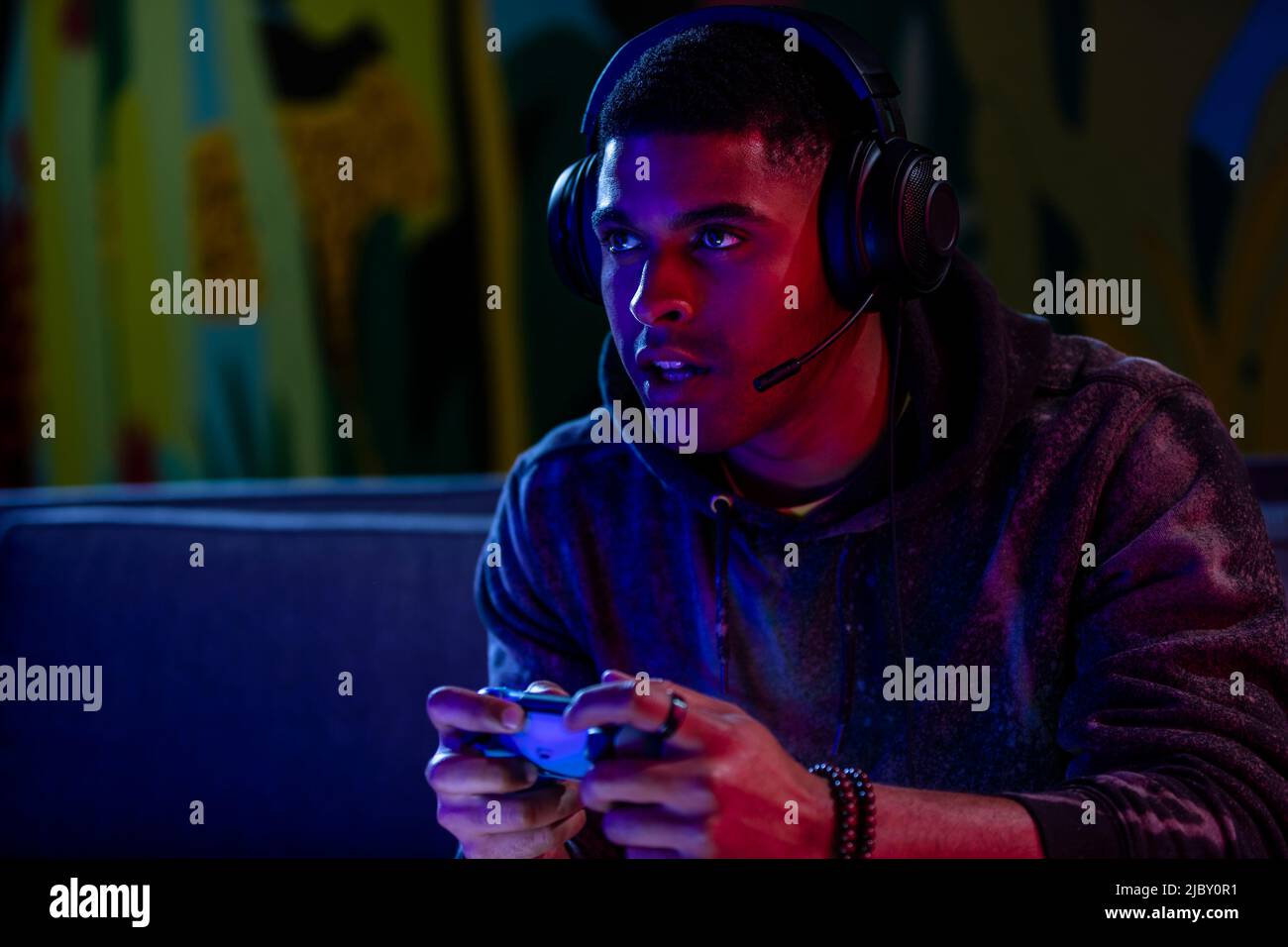 Uomo nero che indossa le cuffie e parla mentre gioca a un videogioco in una stanza buia Foto Stock