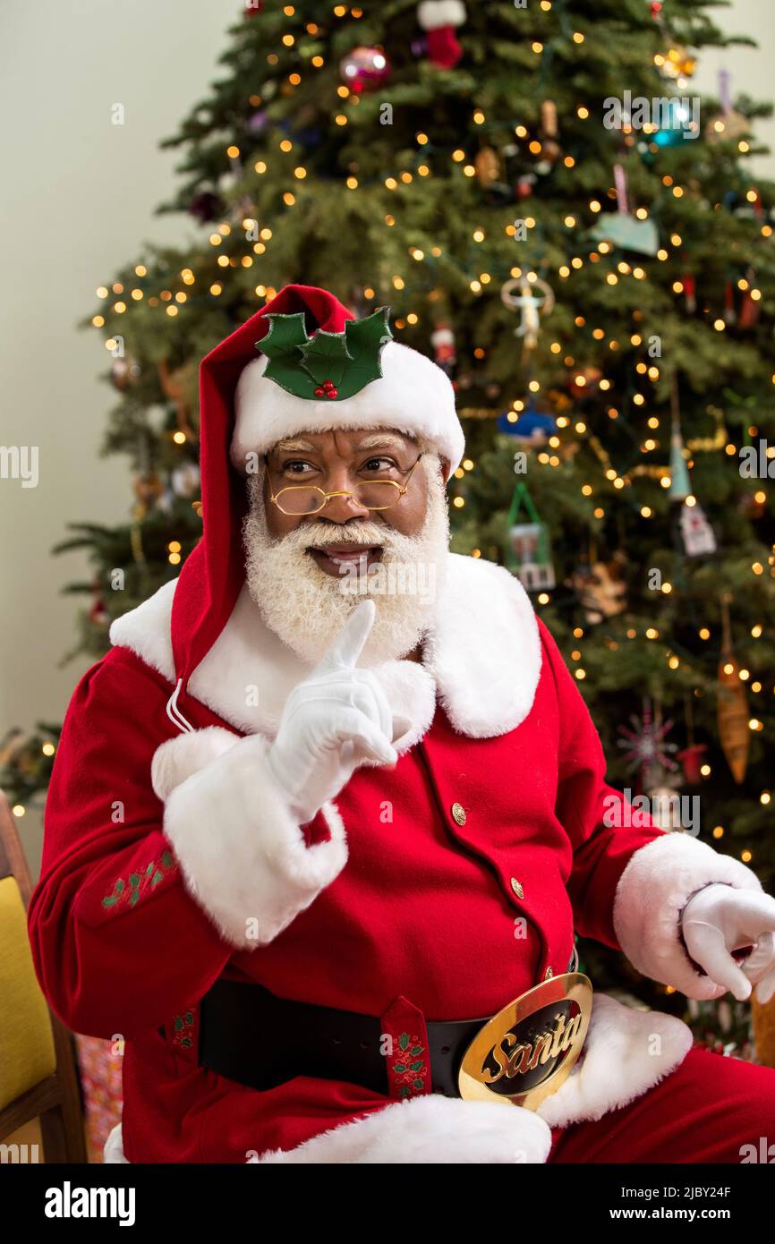 Afroamericano Babbo Natale seduto di fronte all'albero di Natale illuminato. Foto Stock