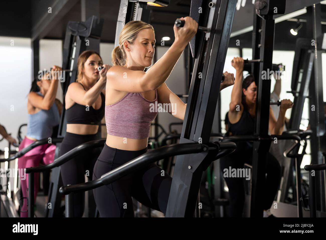 Gruppo di giovani donne atletiche che lavorano insieme in una classe sulle macchine da ginnastica. Foto Stock