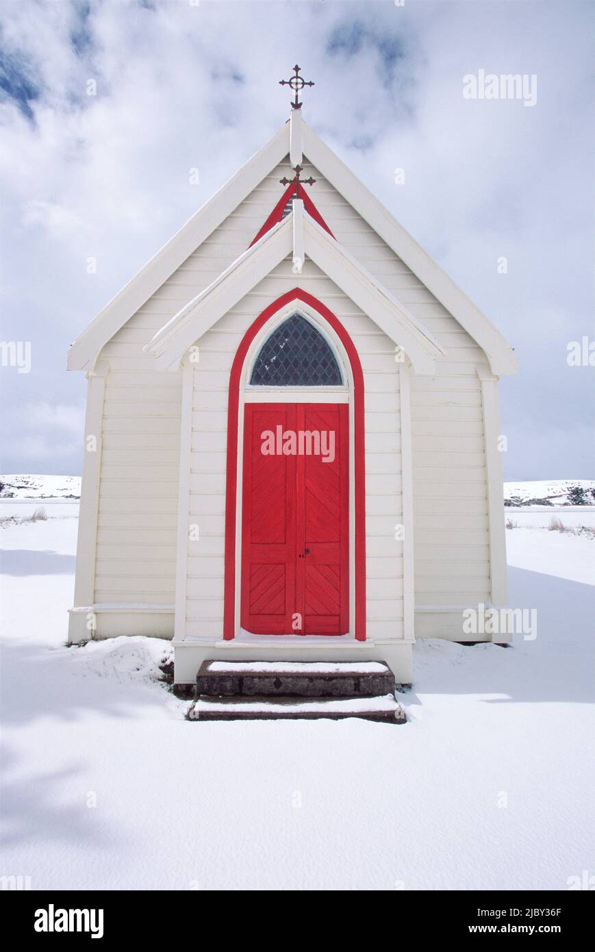 Vecchia chiesa in legno con porta rossa tra il paesaggio innevato Foto Stock