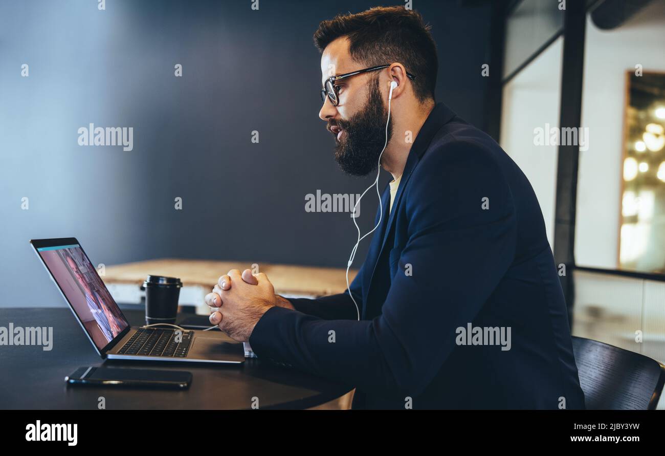 Uomo d'affari moderno che partecipa a una riunione virtuale su un laptop. Giovane imprenditore che indossa le cuffie durante una videochiamata in ufficio. uomini d'affari Foto Stock