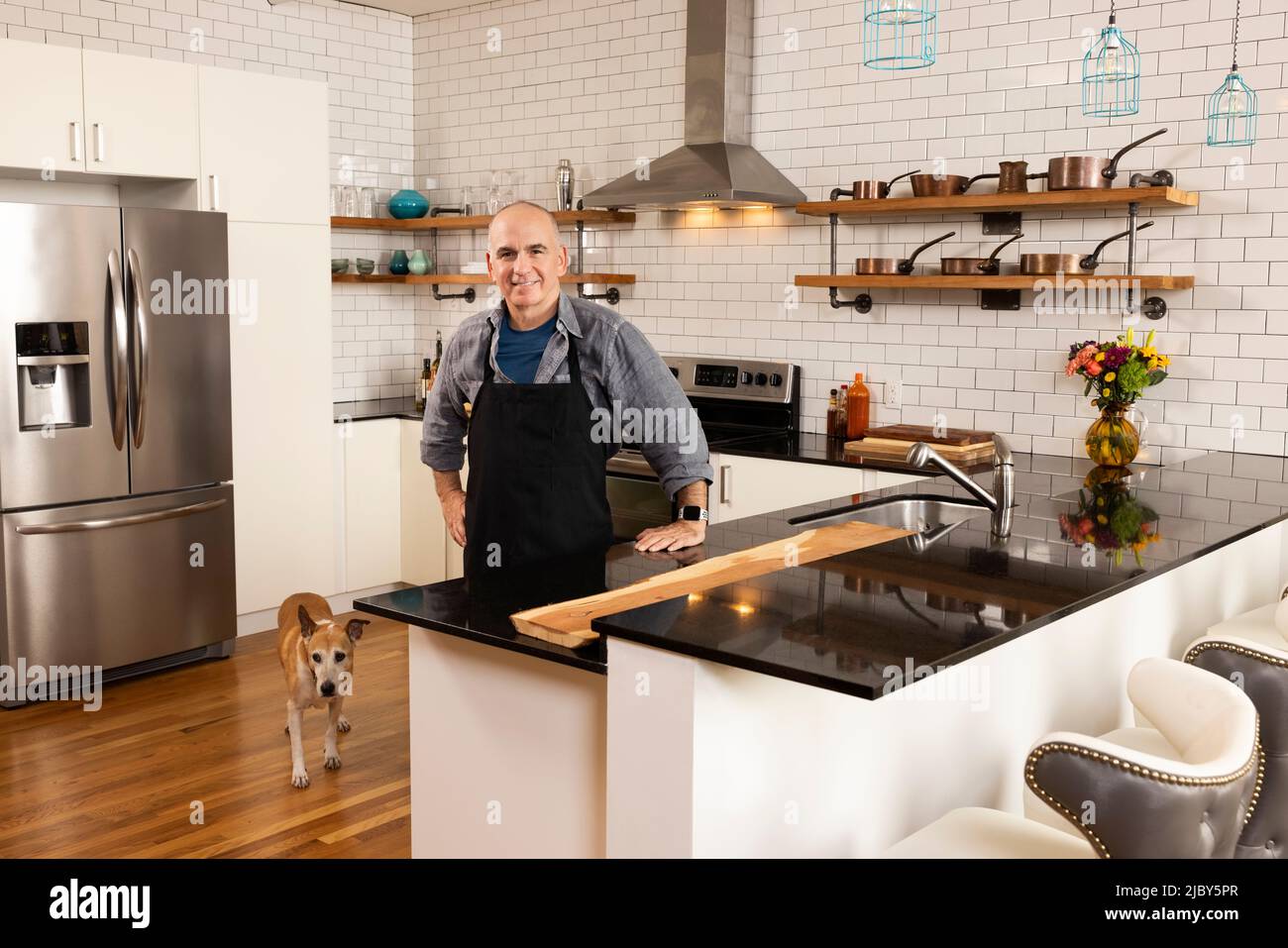 Ritratto di uomo che indossa grembiule in cucina con il suo cane accanto a lui, guardando in macchina fotografica con fiducia. Foto Stock