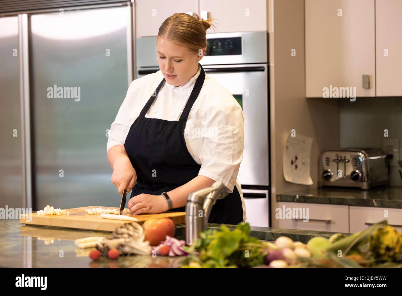 Chef professionista Megan Gill in cucina guardando verso il basso mentre si tagliano le verdure. Foto Stock