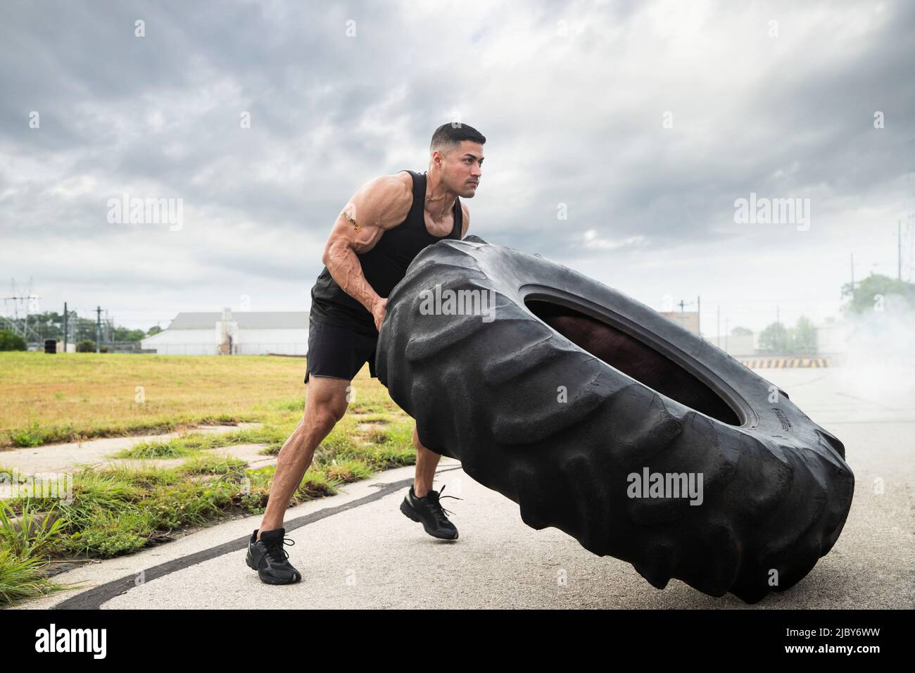 Uomo ispanico muscoloso che indossa la canotta con tatuaggio "forte" sulla sua bicipite, flipping trattore pneumatico Foto Stock