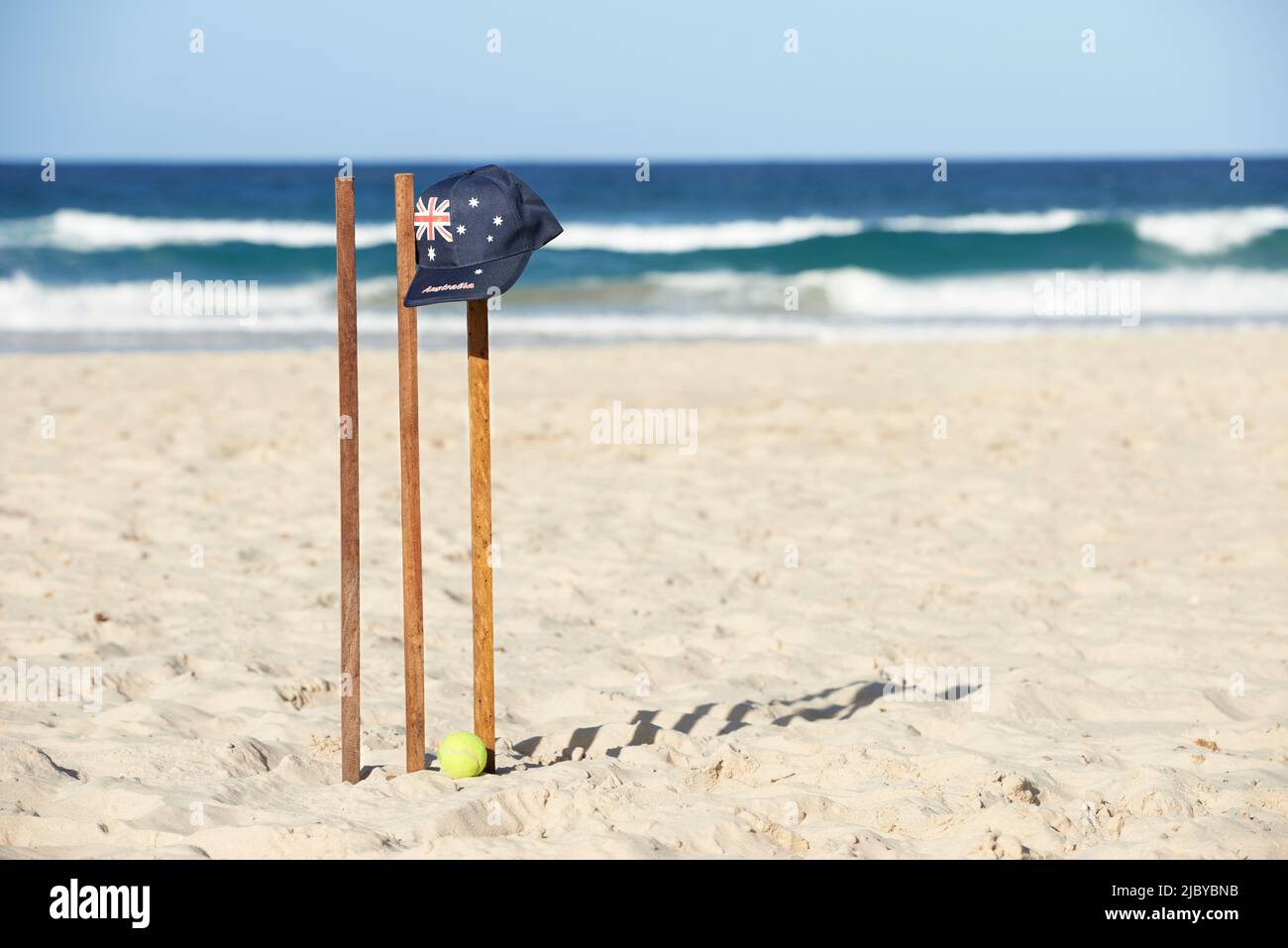 Berretto con bandiera australiana poggiato su ceppi di cricket in legno e palla da tennis in spiaggia Foto Stock