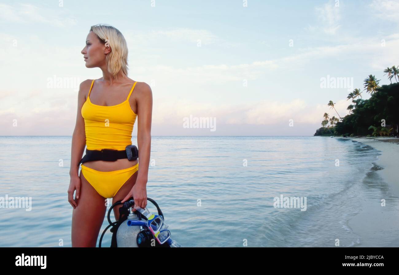 Giovane donna in piedi sulla spiaggia tropicale tenendo il suo equipaggiamento per immersioni subacquee Foto Stock