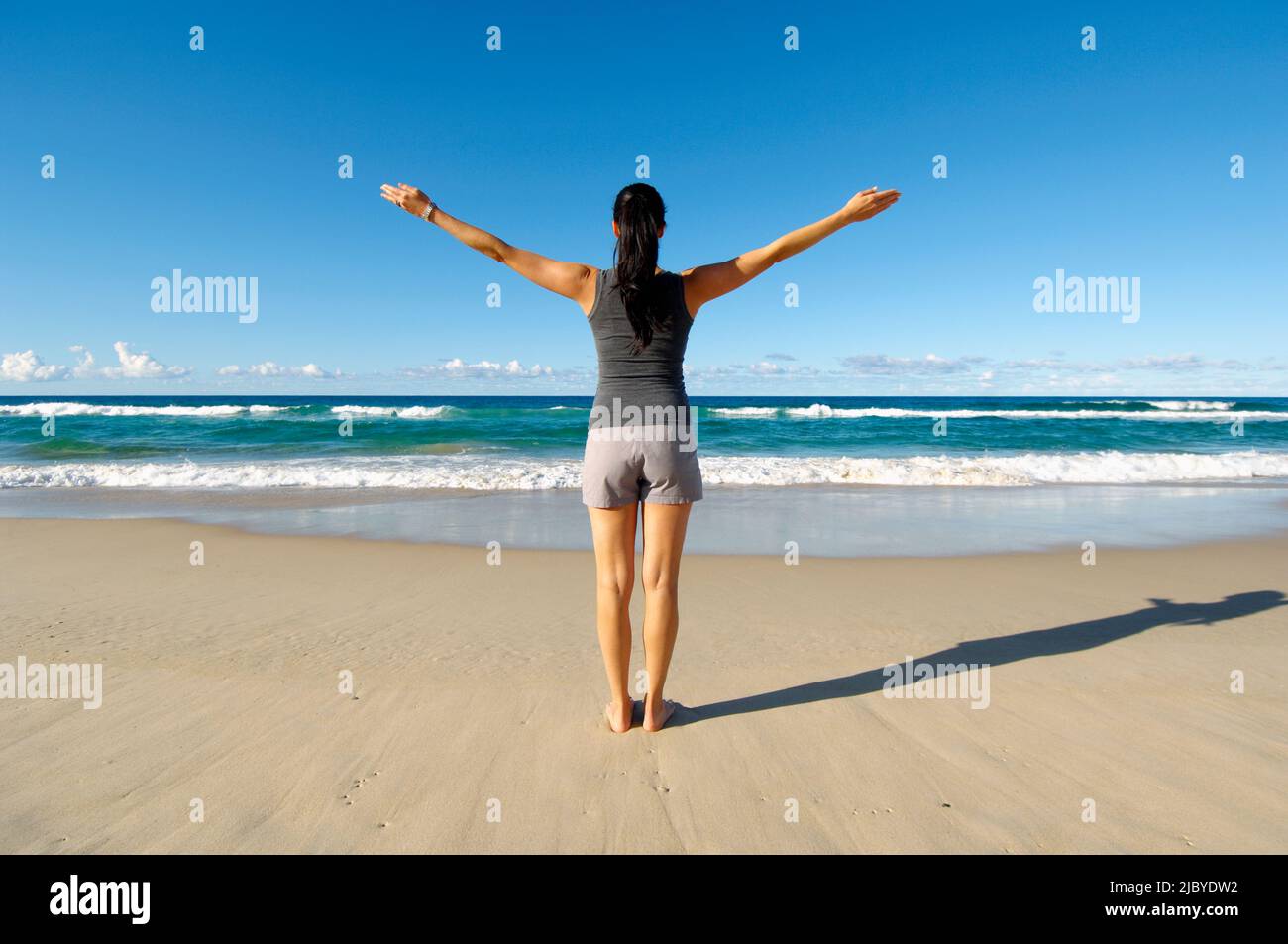 Vista posteriore della donna in piedi sulla sabbia e guardando verso il mare con le braccia distese Foto Stock