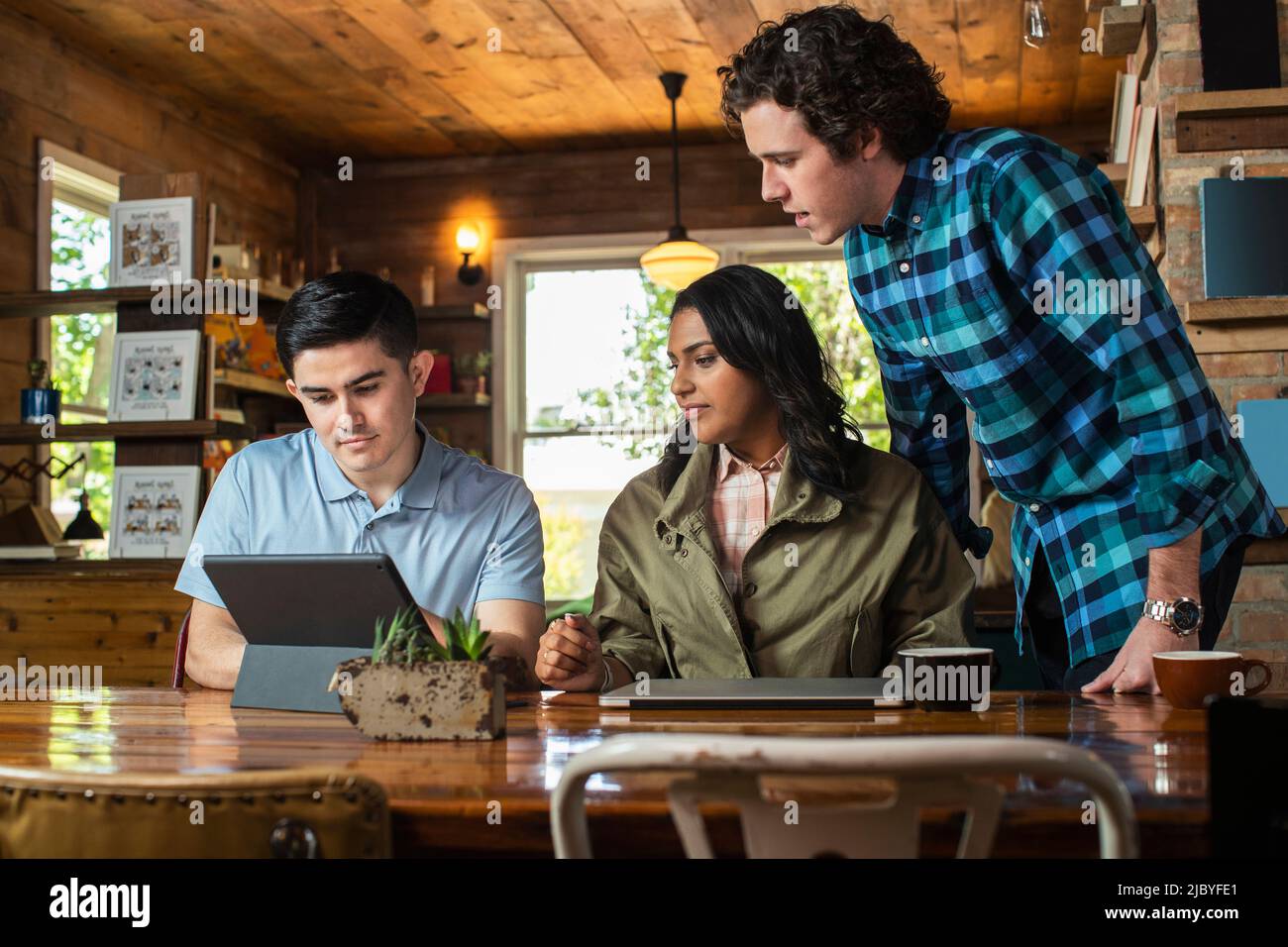 Gruppo di giovani adulti al tavolo nella libreria del coffee shop che hanno discusso con il tablet digitale e il computer portatile Foto Stock