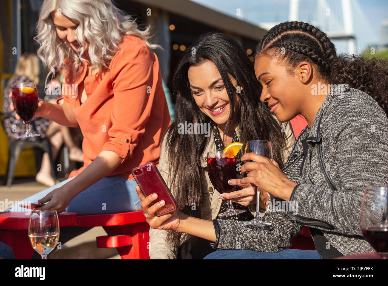 Gruppo di giovani collaboratori che si affacciano sul patio all'aperto e che bevono bevande per l'happy hour, due ragazze che guardano il telefono cellulare Foto Stock