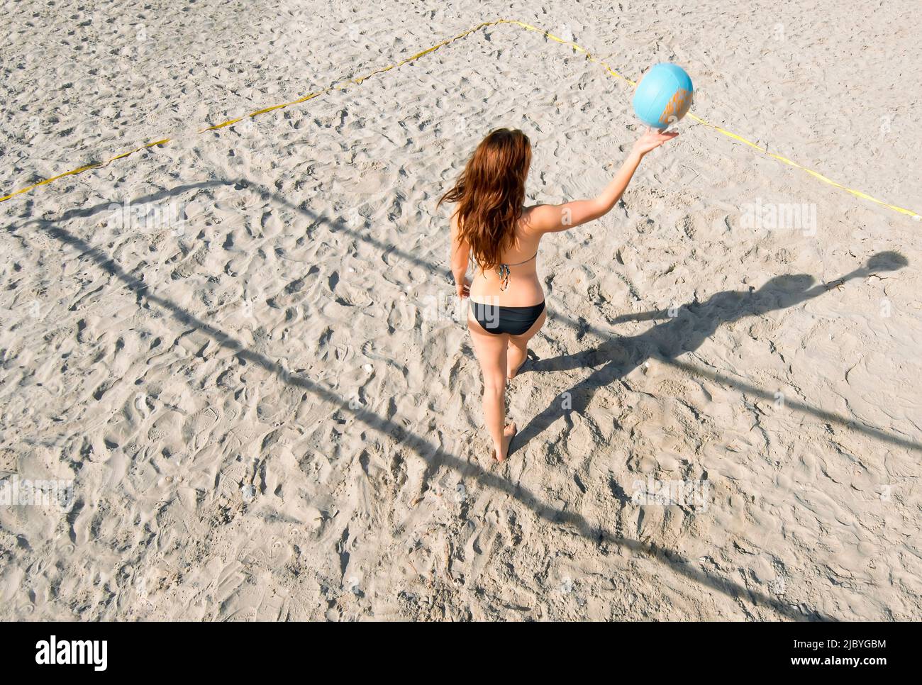 Vista posteriore del giovane giocatore di pallavolo che rimbalza sulla palla mentre cammina sulla sabbia Foto Stock