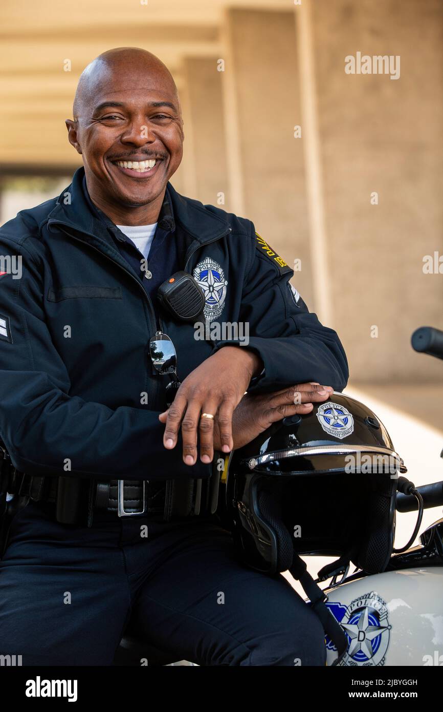 Ritratto di ufficiale di polizia seduto sul suo motociclo esterno guardando verso la macchina fotografica sorridente Foto Stock