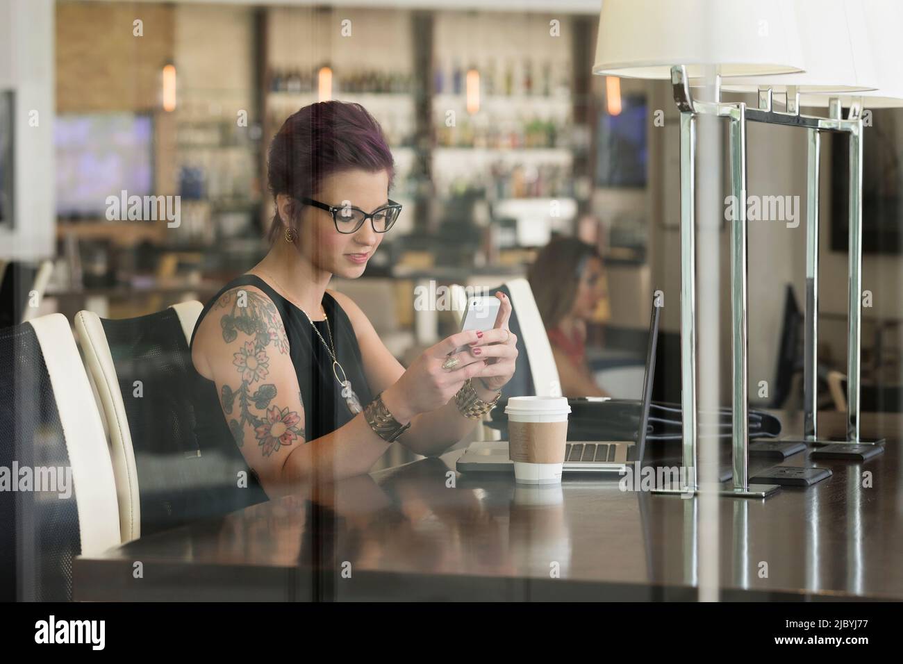 La donna caucasica mediante telefono cellulare e computer portatile in coffee shop Foto Stock