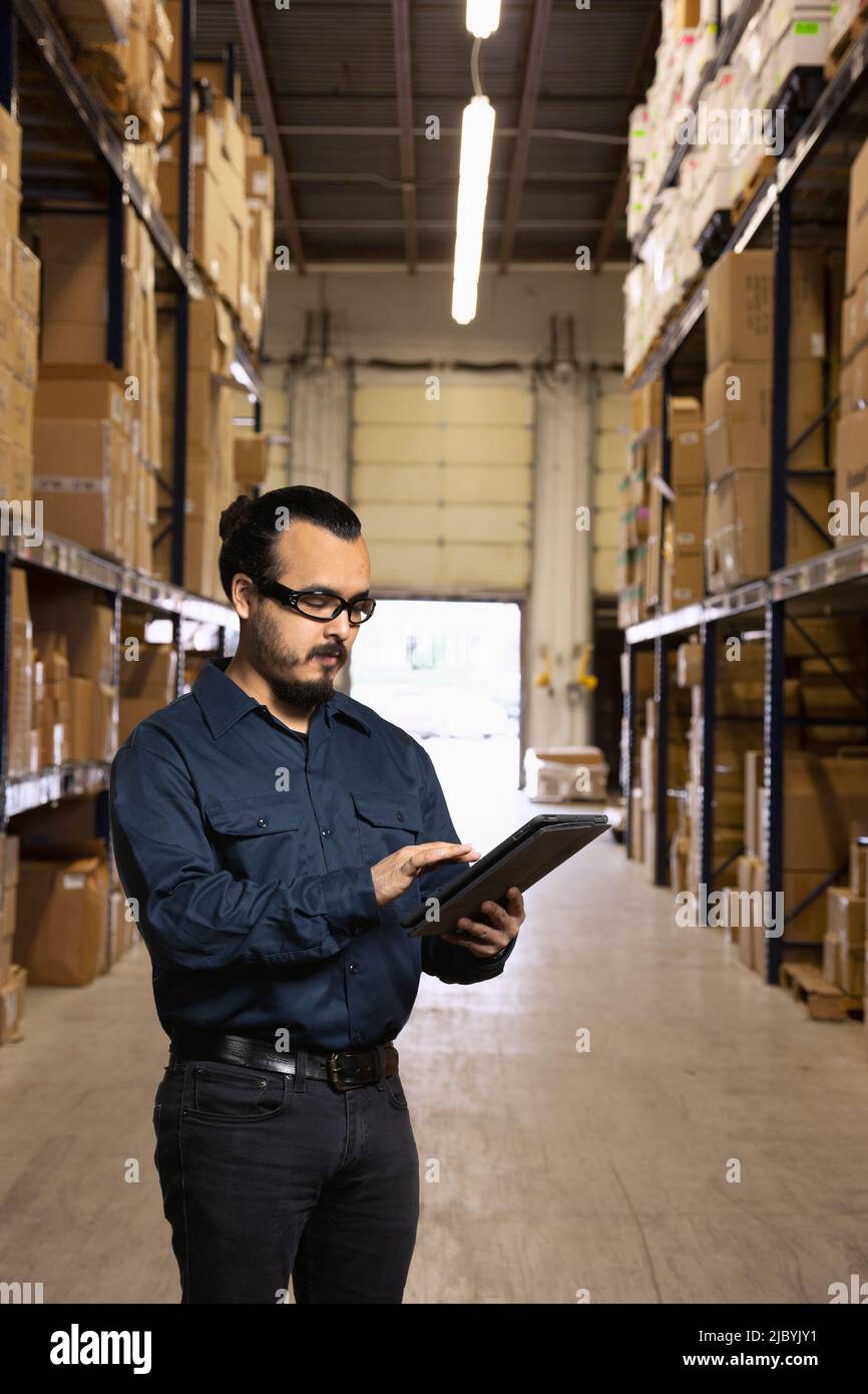 Giovane magazzino ispanico che lavora a digitare in tablet Foto Stock