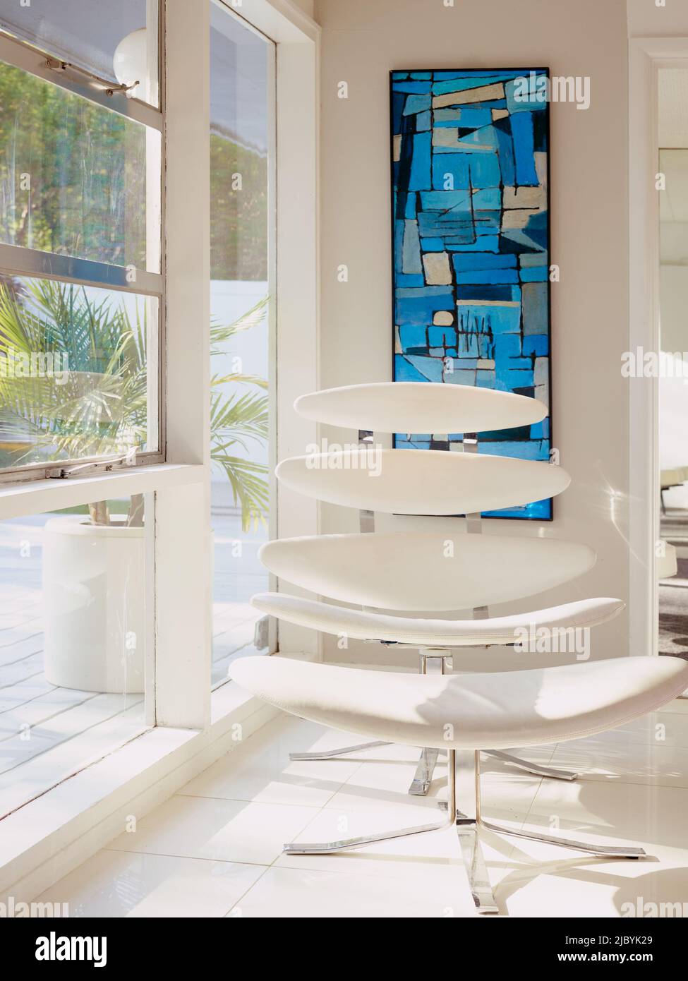 Sedia bianca di metà secolo in un angolo con finestre dal pavimento al soffitto. Foto Stock