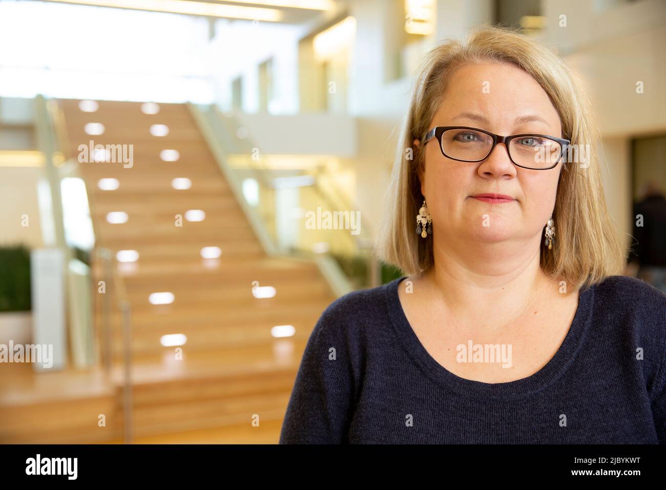 Ritratto di donna di mezza età con vetri in piedi dalla scala nella lobby dell'edificio, sorridente guardando verso la macchina fotografica Foto Stock