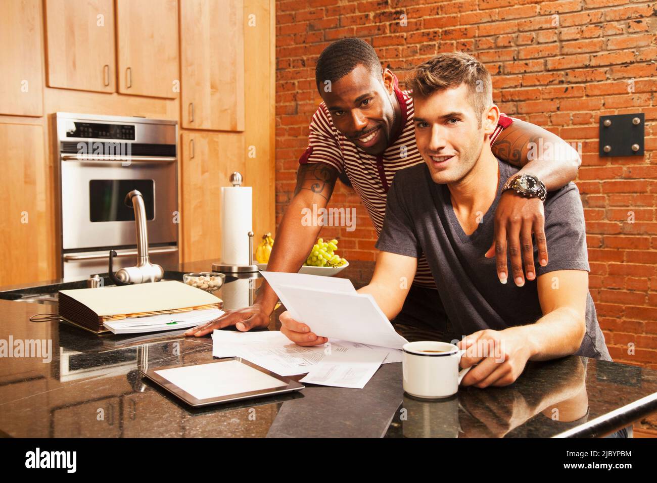 Coppia gay che guarda la documentazione in cucina Foto Stock