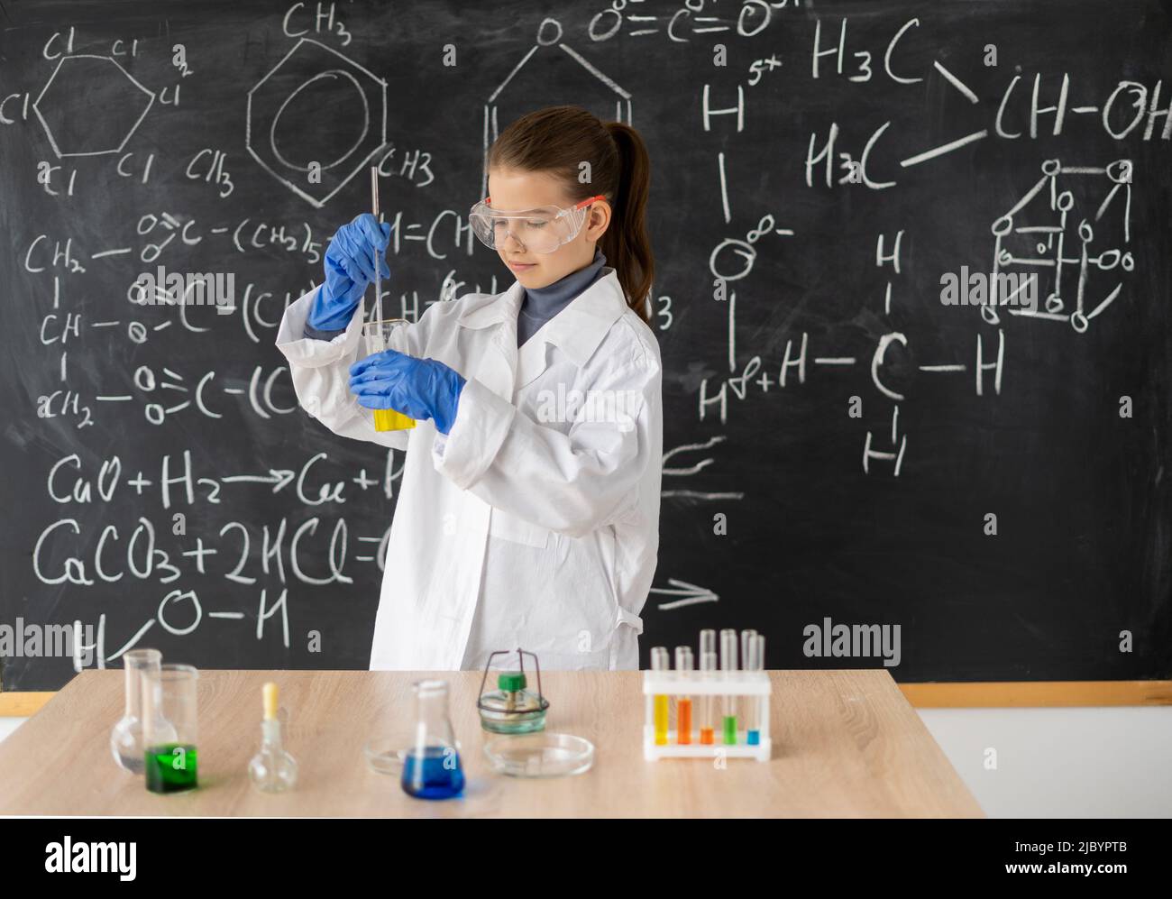 giovane studentessa chimica in un cappotto bianco fa un esperimento chimico in una lezione di chimica, di nuovo a scuola Foto Stock