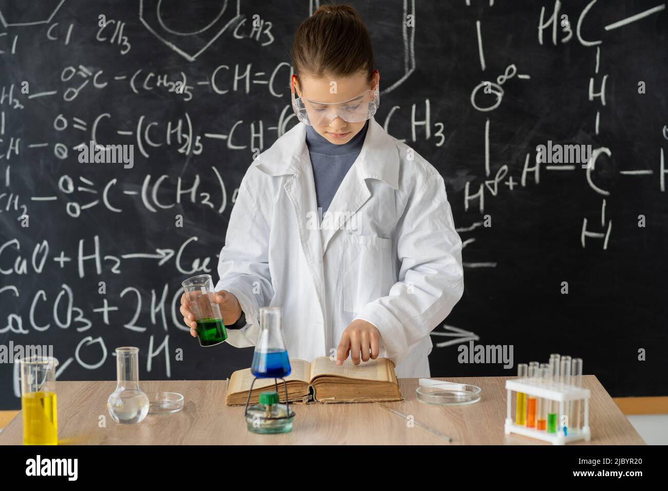 giovane adorabile studentessa ragazza che scrive un risultato di chimica sul libro mentre fa un esperimento scientifico e in piedi nel laboratorio moderno con Foto Stock