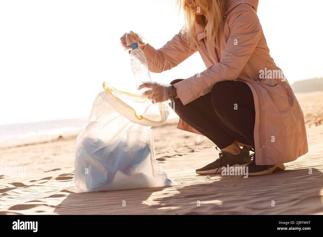 Donna coccolata assistente che aiuta a pulire spiaggia sabbiosa da rifiuti di plastica, spazzatura. Cambiamento climatico problema ecologico. Foto Stock