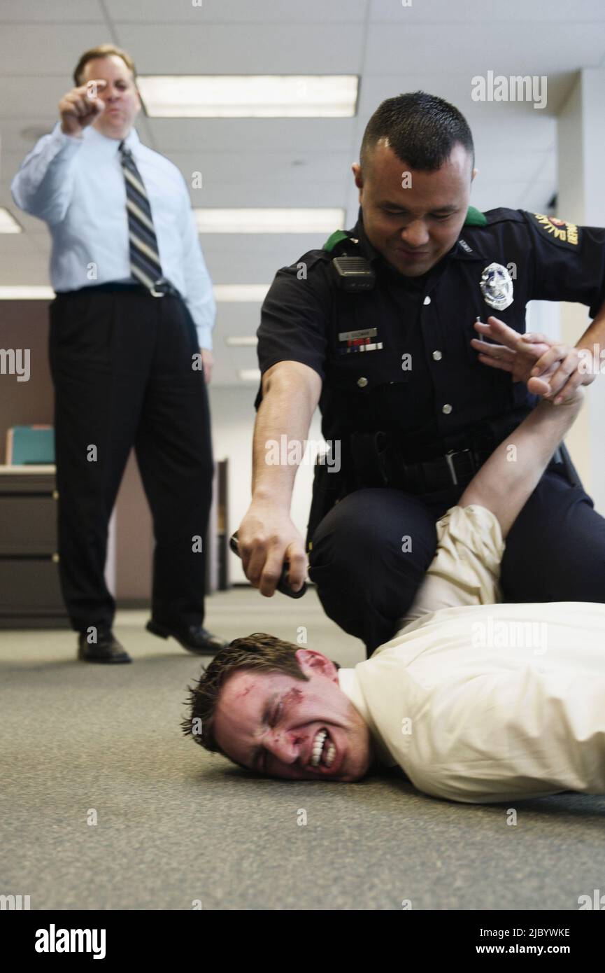 Funzionario di polizia holding battuto l uomo d affari sul pavimento in office Foto Stock