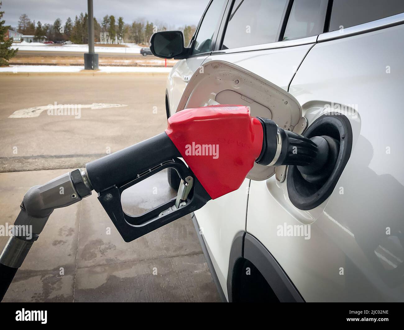 Pompa del gas ugello del carburante con manico rosso che riempie il serbatoio dell'auto bianca in Minnesota. Concetto di prezzo del gas elevato. Foto Stock