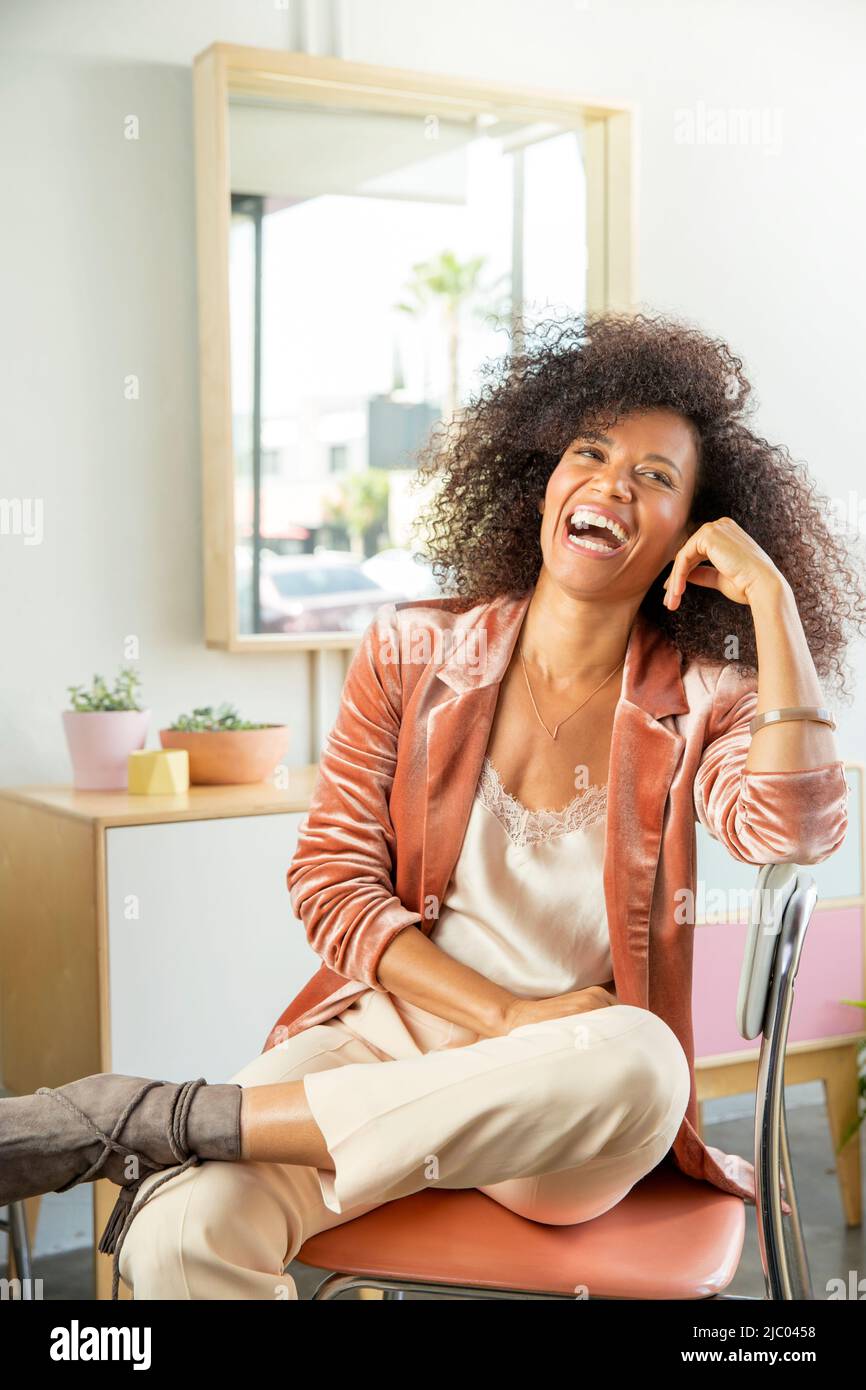 Una donna di mezza età si appoggia in una sedia e ride. Foto Stock