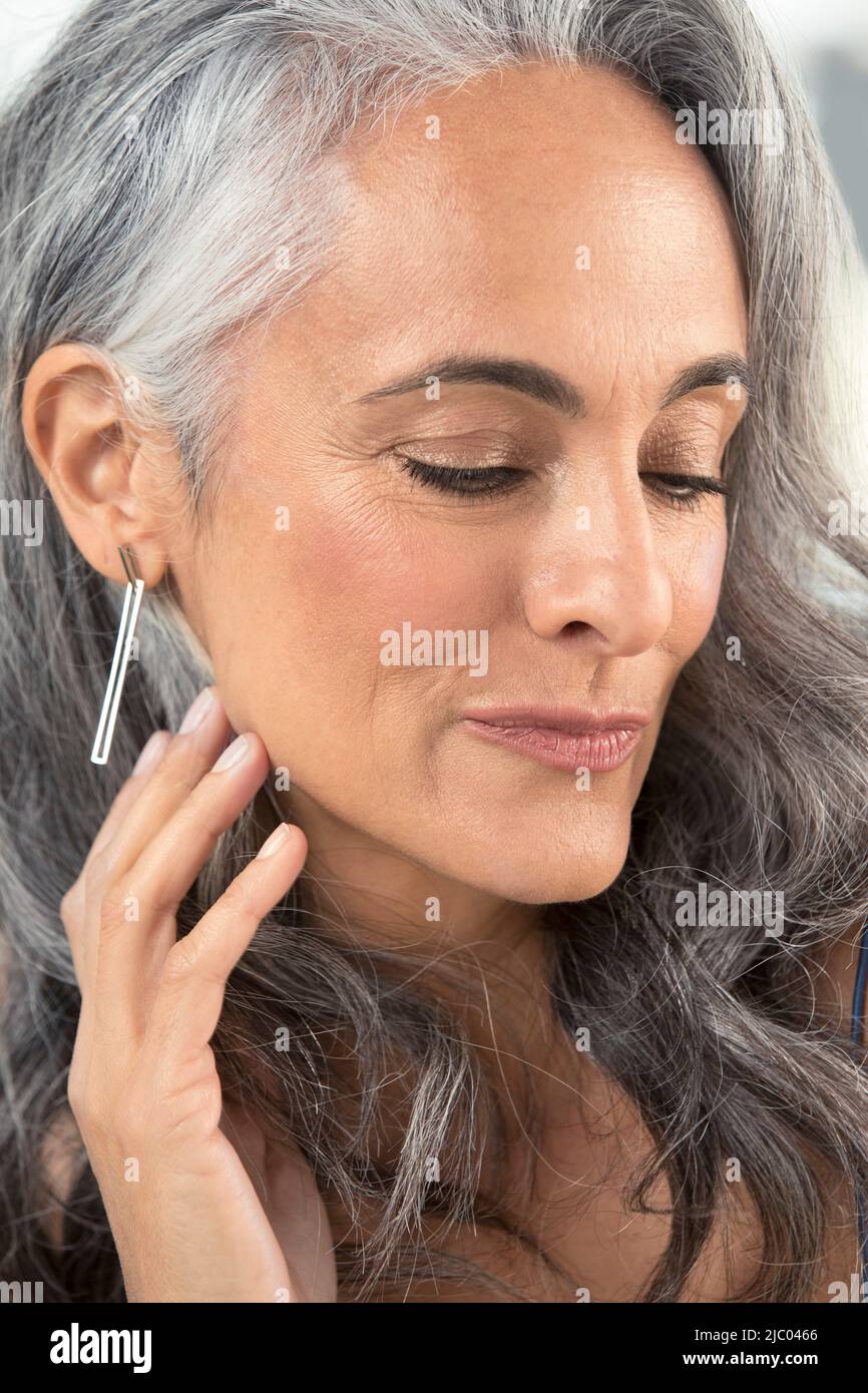 Una donna di mezza età dall'aspetto giovane e calmo guarda dalla fotocamera mentre tira i capelli dietro l'orecchio. Foto Stock