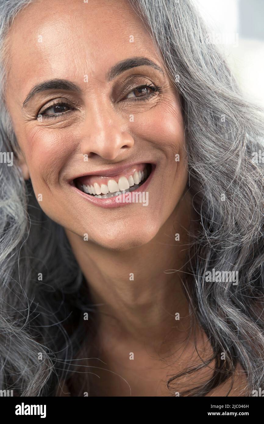 Giovane donna di mezza età con capelli grigi guarda fuori dalla fotocamera con un grande sorriso toothy Foto Stock