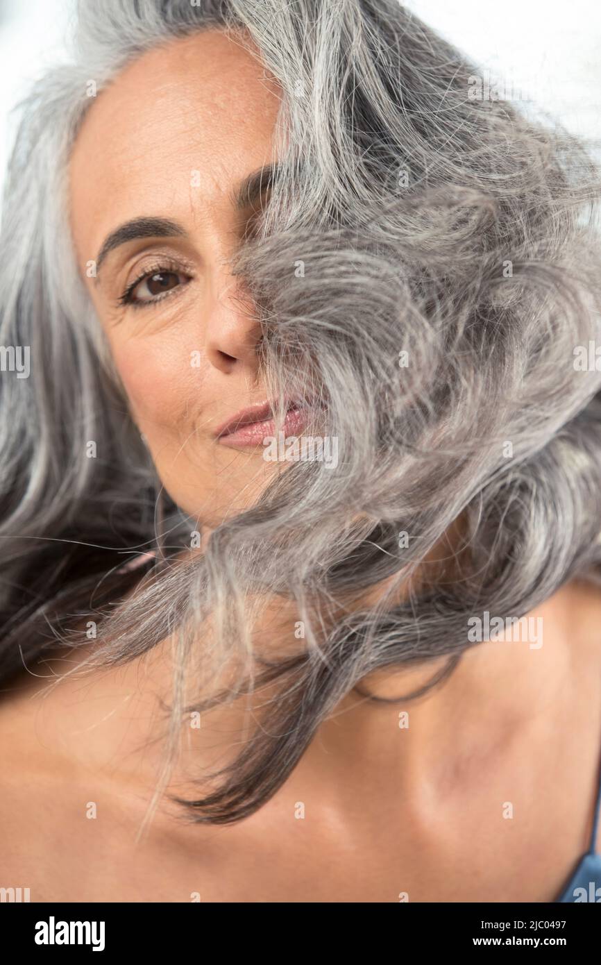 Ritratto di una giovane donna di mezza età che guarda in macchina fotografica, capelli che soffiano sul suo volto. Foto Stock