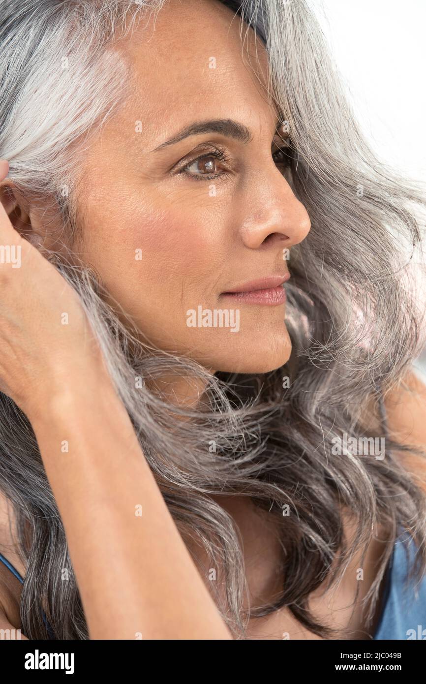 Una donna di mezza età con capelli grigi tira i capelli dietro l'orecchio Foto Stock