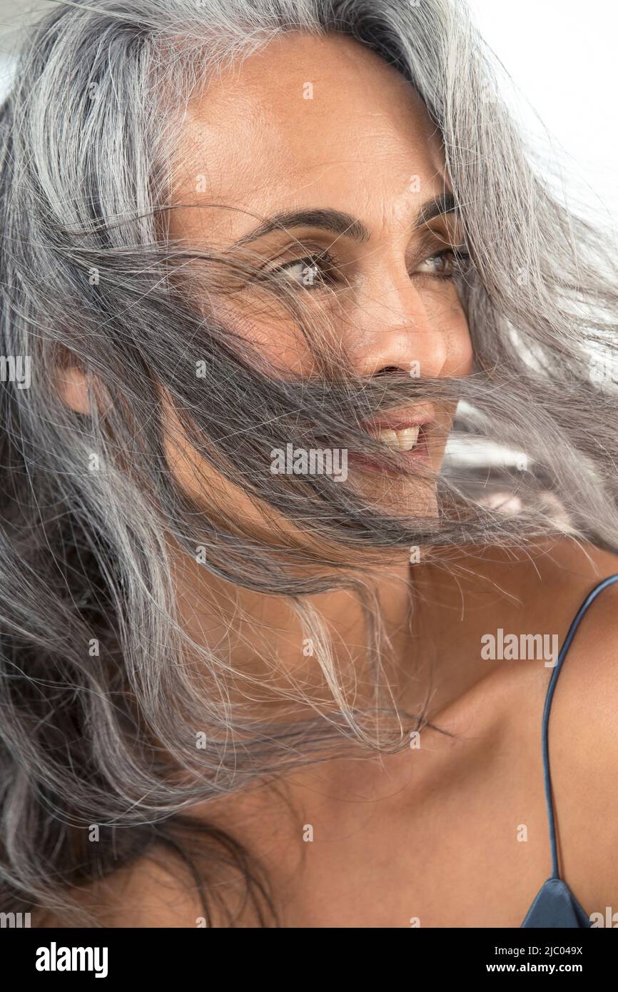 Una giovane donna di mezza età guarda a destra come il vento soffia i suoi capelli grigi attraverso il suo viso. Foto Stock