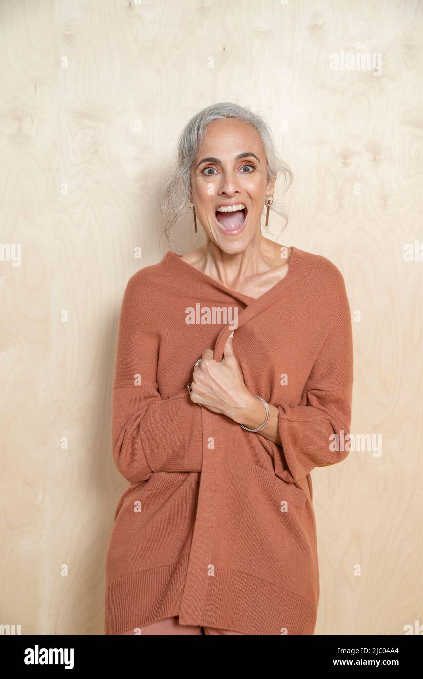 Giovane donna di mezza età chiude il suo maglione e ride in macchina fotografica. Foto Stock