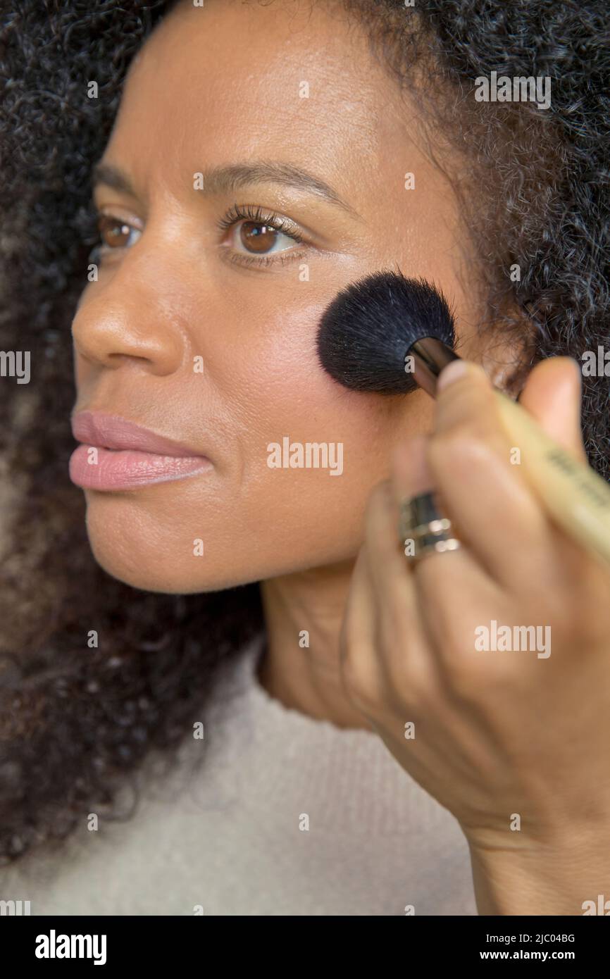 Gara mista, donna di mezza età guarda fuori dalla fotocamera mentre si mette sul make up. Foto Stock