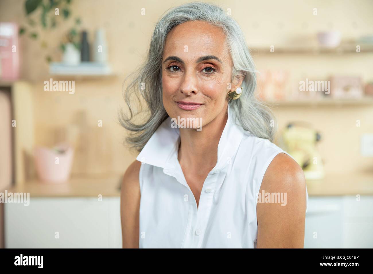 Primo piano ritratto di una donna di mezza età con capelli grigi naturali guardando la fotocamera con un sorriso caldo. Foto Stock