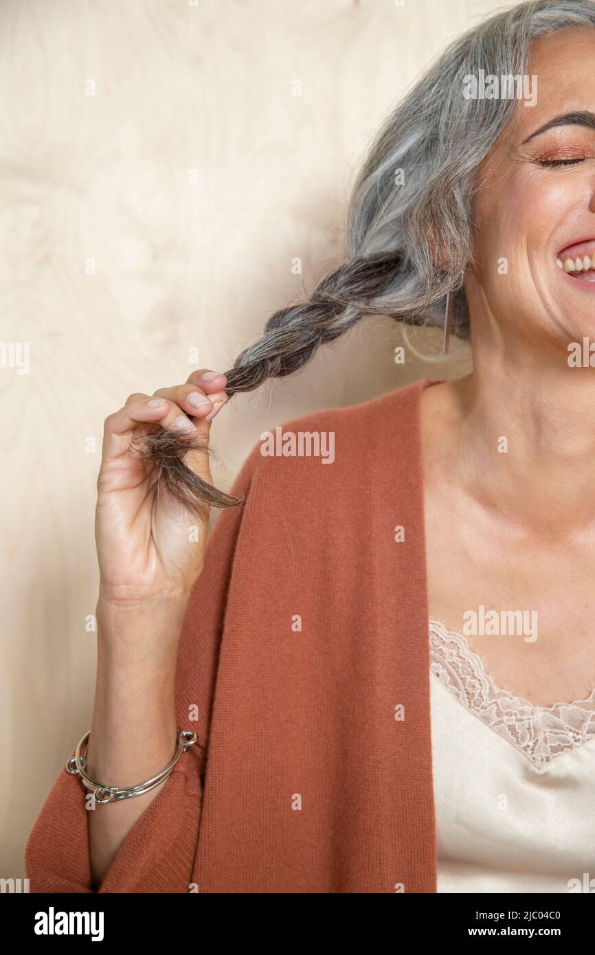Primo piano di una donna di mezza età con capelli grigi che tengono la sua coda di pony fuori di lato, ridendo. Foto Stock